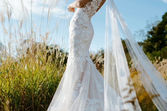 Braut in einem eleganten, aus lacy und satin bestehenden Kleid steht im Freien.