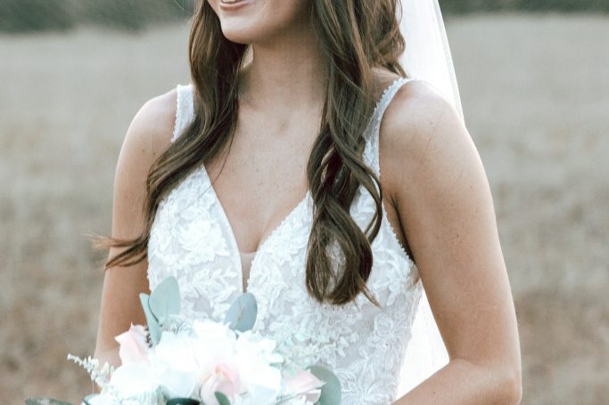 Braut mit langem Haar und einem Brautstrauß, trägt ein elegantes, weißes Kleid.