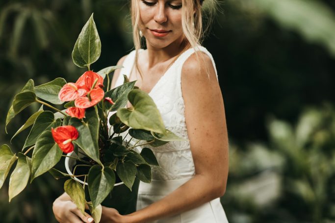 Braut mit Blumenstrauß aus roten Anthurien in einem natürlichen Umfeld.